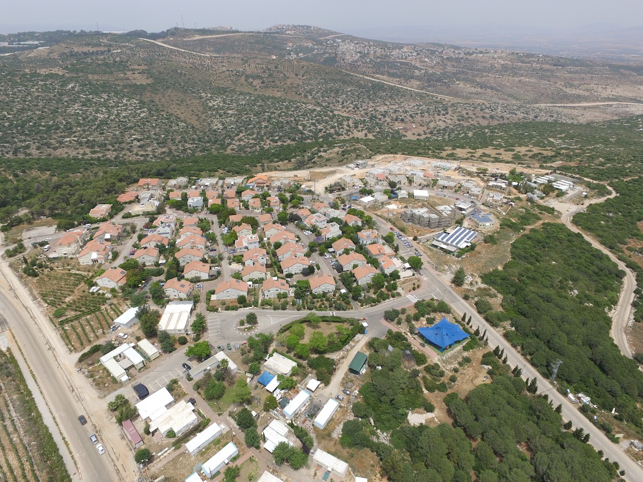 מבט אווירי על היישוב טל מנשה — בתים עם גגות רעפים אדומים בין חורש וגבעות